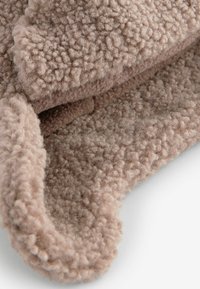 Tissu doux et texturé de couleur beige clair, affichant une surface duveteuse et pelucheuse avec un bord enroulé pour la chaleur et le confort.