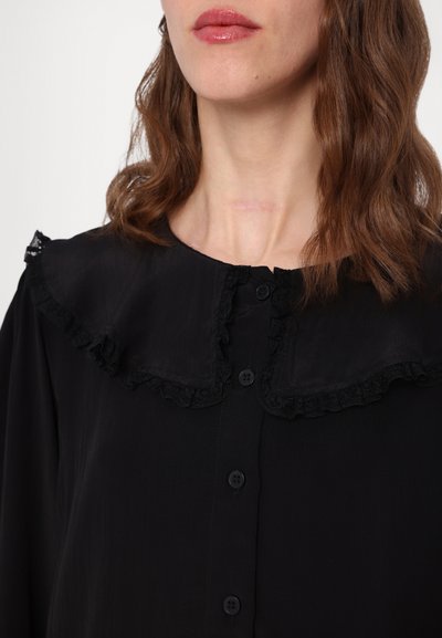 Black blouse with a ruffled lace collar and button front. Features smooth fabric and a relaxed fit.