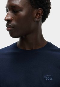 Camiseta de algodón en color azul marino con un bordado de un oso en azul claro en el lado izquierdo del pecho; cuello redondo y mangas cortas, textura suave.