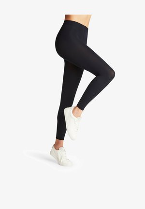 Des leggings noirs en matière extensible, dotés d'une taille haute et d'une texture lisse, associés à des baskets blanches.
