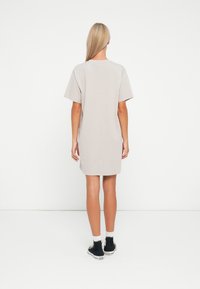 Light gray dress made of cotton, featuring a relaxed fit, short sleeves, and a straight hem. Worn with black sneakers and white socks.