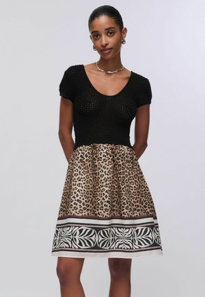 Giovane donna che indossa un top nero a maniche corte in maglia con gonna leopardata con bordo decorativo nero e bianco.