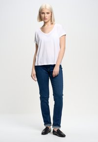Vit kortärmad t-shirt med V-hals, blå jeans med uppvikt fåll och svarta loafers. Enkel, avslappnad passform, mjuk tygtextur.