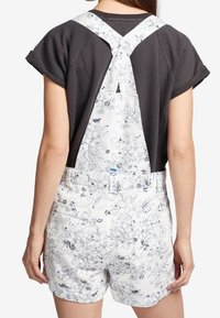 Salopette blanche à motifs floraux avec bretelles réglables, associée à un chemisier noir à manches courtes. Matériau en coton ; design décontracté.