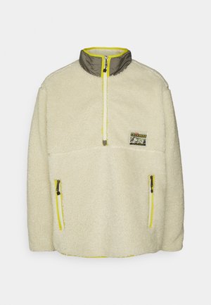 Pull en polaire crème avec un col gris contrastant. Comprend des zips jaunes et une poche plaquée à l'avant. Texture douce avec un look douillet.