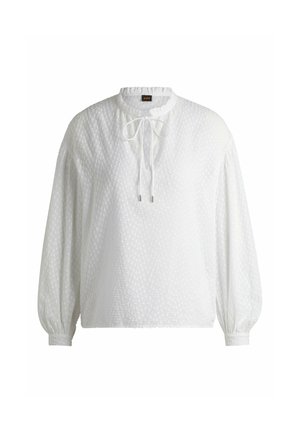 Blusa bianca a maniche lunghe con un motivo testurizzato, scollatura rotonda e chiusura a cravatta sul davanti; polsini elasticizzati e vestibilità rilassata.