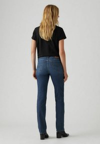 Blue denim jeans, straight leg design, medium wash, visible back pockets with distinctive stitching, paired with a black short-sleeve shirt.