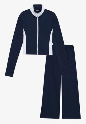 Navy two-piece tracksuit featuring a cropped, zip-up jacket with white accents and wide-leg pants with an elastic waistband.