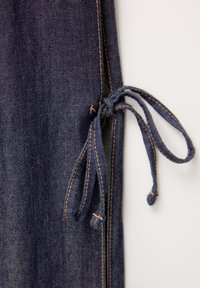 Blå denimtyg med en knutdetalj. Har kontrasterande orange sömmar längs sömmarna och har en slät textur.