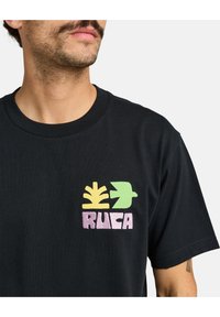 Zwarte katoenen t-shirt met kleurrijke geborduurde graphics: een gele plant, een groene vogel en de tekst "RUCA" in het roze. Korte mouwen en een ronde hals.