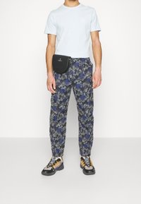 T-shirt bleu clair à manches courtes, pantalon navy à motifs floraux, sac à main noir et baskets noires avec des lacets jaunes.