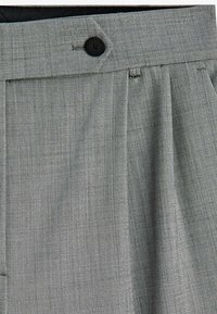 Gros plan sur un pantalon gris sur mesure avec une ceinture à bouton noir et un détail en tissu plissé.
