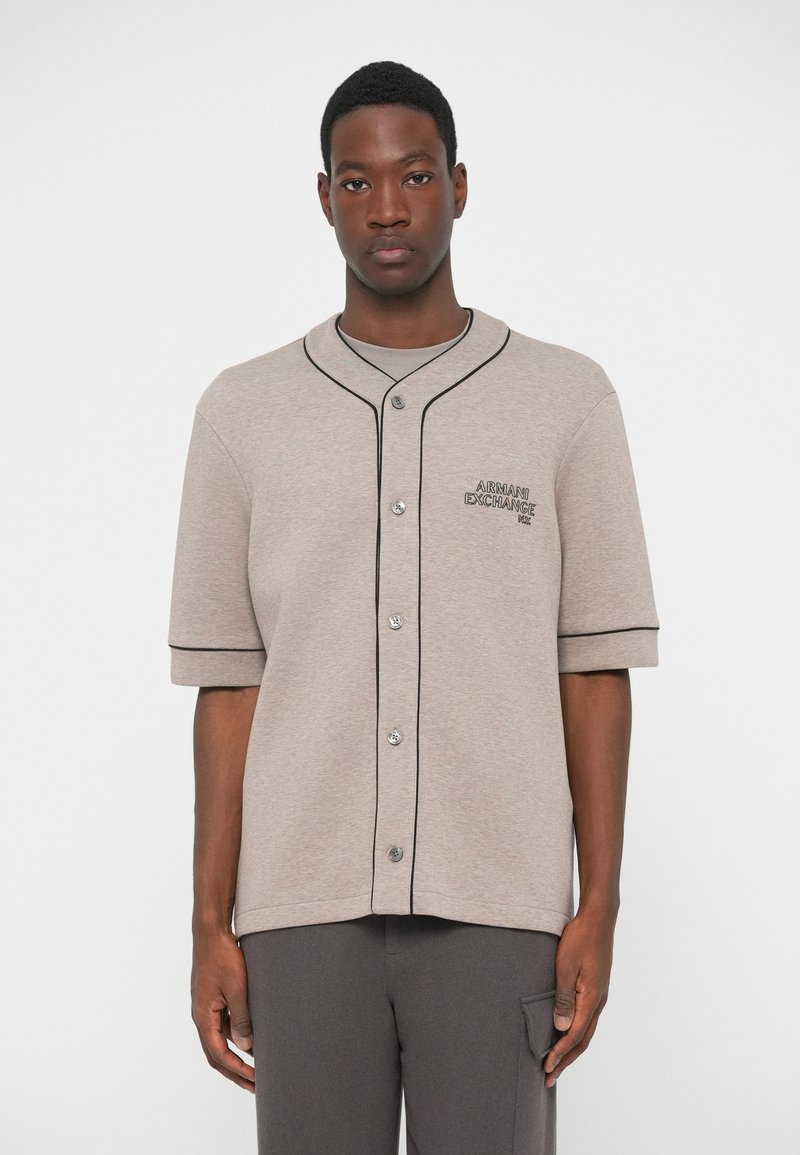 Camicia a maniche corte color marrone chiaro con bottoni, rifiniture nere e dettaglio del logo ricamato. Realizzata in tessuto morbido e testurizzato.