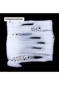 Hvit skum med bobler på en svart bakgrunn, som viser en glatt, teksturert overflate. Inkluderer hashtaggen #VitaminColor.
