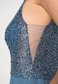 Blå klänning med en pärlad livstycke med ett nätpanel, V-halsdesign och en flödande kjol som visar upp intrikat pärlbroderi och textur.