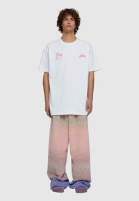 Balta didelė T-shirt su rožine tekstūra, derinama su plačiais, gradientiniais rožiniais ir violetiniais džinsais, turinčiais tekstūrinį paviršių.