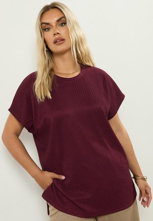 T-shirt bordeaux a righe con maniche corte, scollatura rotonda, spacchi laterali e vestibilità rilassata. Il materiale appare liscio e tessurizzato.