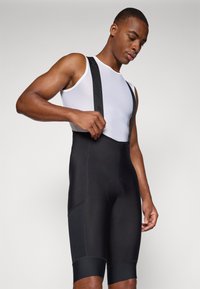 Schwarze Radsport-Bib-Shorts aus glattem, elastischem Stoff mit Netzträgern, ausgestattet mit einem gepolsterten Sitz und kontrastierenden schwarzen Nähten.