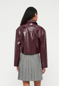 Bordo lažna usnjena krajša jakna z sijočim zaključkom in izrazitimi šivi na ramenih, kombinirana z nabrano črno-belo karo krilo.