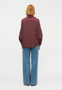 Chemise à manches longues rayée rouge et blanche, coupe ample avec poignets à boutons, portée avec un jean large bleu clair, vue de dos.