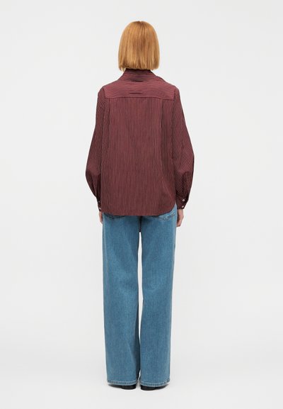 Chemise à manches longues rayée rouge et blanche, coupe ample avec poignets à boutons, portée avec un jean large bleu clair, vue de dos.