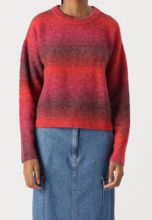 Woman wearing a fuzzy, gradient red to purple long-sleeve sweater paired with a high-waisted blue denim skirt with front pockets.