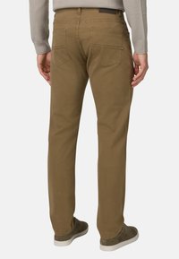 Pantalones de algodón marrón con un diseño de pierna recta. Presentan dos bolsillos traseros y una etiqueta en la cintura. Combinados con un suéter gris texturizado y zapatos.
