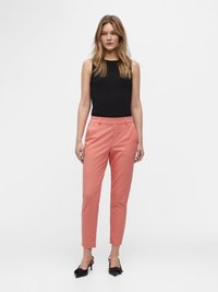 Zwarte mouwloze top, licht koraalkleurige Tailor-pants met frontzakken en taps toelopende pijpen, gecombineerd met zwarte hakken. Eenvoudig ontwerp, gladde textuur.
