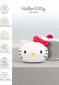 Hello Kitty-shaped white silicone facial cleansing brush with red bow, waterproof and dermatologist-approved, shown on a gray surface.
