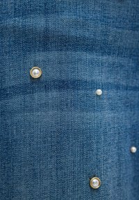 Jasnoniebieska tkanina dżinsowa o fakturowanej powierzchni, ozdobiona złotymi ćwiekami z białymi perłami. Ćwieki są rozproszone po tkaninie.