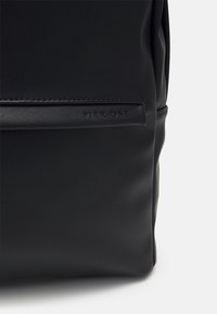 Musta nahkareppu, joka on sileäpinnotteinen ja jossa on kohokuvioitu "PIER ONE" -logo sivupaneelissa.