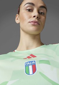 Zeleno kamuflažno majico z rdečimi detajli in logotipom italijanske nogometne zveze FIGC. Izdelana je iz sintetičnega materiala z okroglim izrezom.