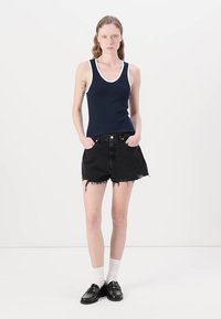 Marineblå tanktop med hvite kanter, i kombinasjon med svarte denimshorts med frynser. Modellen har på seg svarte loafers og hvite sokker.