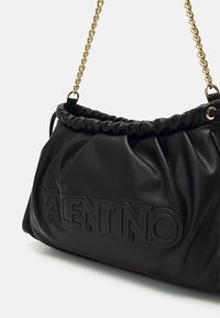 Bolso negro de cuero de Valentino con borde superior fruncido y correa de cadena dorada para el hombro, logo en relieve visible en el lado frontal.