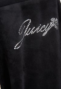 Crni velur tkanina s sjajnim kristalnim "Juicy" logotipom, glatke teksture i suptilnim sjajem.
