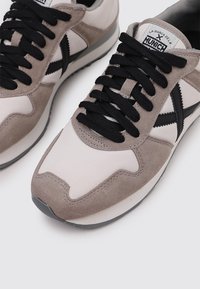 Sneakers with a suede and textile upper, featuring a light grey and beige color scheme. Black laces and accents complete the design.
