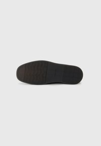 Suela de zapato de goma negra con patrón de agarre texturizado y diseño plano. Presenta una marca en el lateral. Acabado liso con bordes definidos.