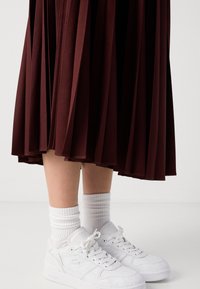 Jupe midi plissée bourgogne au tombé fluide, associée à des baskets blanches et des chaussettes blanches retroussées. Design minimaliste et texture douce.