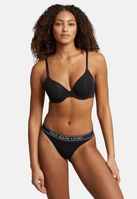 Zwarte push-up bh met dunne verstelbare bandjes en bijpassende string met een witte logo band rond de taille. Gladde stoftextuur.