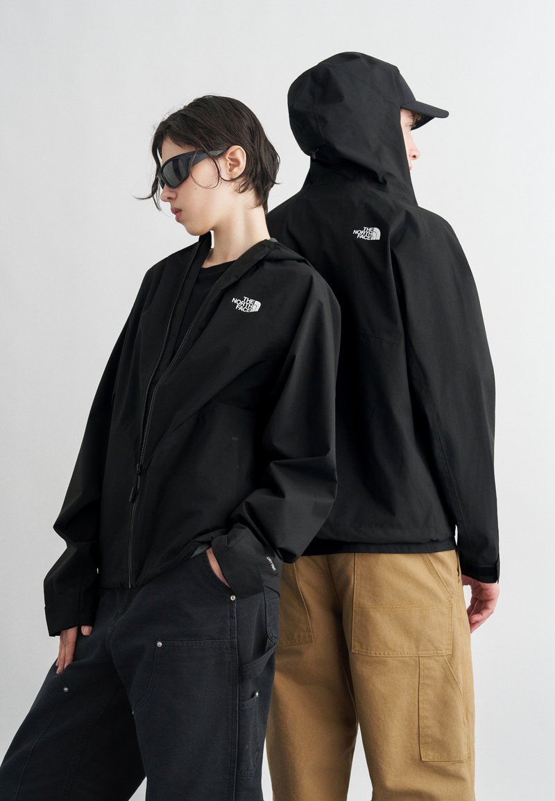 Δύο άτομα φορούν μαύρα μπουφάν The North Face, το ένα κοιτάει μπροστά με γυαλιά ηλίου, το άλλο έχει την πλάτη γυρισμένη, φοράει κουκούλα και καπέλο.