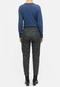 Blue long-sleeve sweater paired with gray plaid trousers. The trousers have an elastic waistband and taper at the ankles. Worn with black block-heel boots.