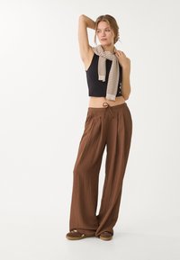 Pantaloni marroni a gamba larga in tessuto texture con vita regolabile a cordoncino. Abbinati a un top corto nero e a una sciarpa leggera a righe.