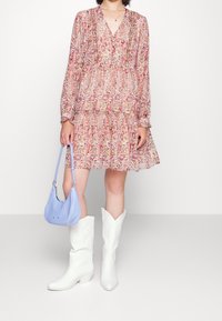 Abito a maniche lunghe con stampa floreale e gonna a strati; abbinato a una borsa blu e stivali da cowboy bianchi con punta e cuciture.
