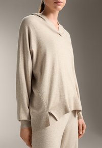 Beige capuchonpullover gemaakt van zachte stof, met een relaxte pasvorm, geribbelde accenten en een gespleten zoom voor extra detail.