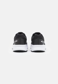 Chaussures de sport noires avec une tige en mesh respirant, une semelle intermédiaire blanche et une semelle extérieure noire texturée pour une meilleure adhérence. Branding minimal sur le côté.