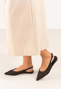 Bailarinas negras de malla tipo slingback con punta afilada, que cuentan con un upper texturizado y un diseño de tira minimalista. Combinadas con una falda de un beige claro.