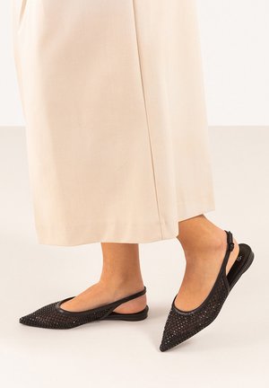 Bailarinas negras de malla tipo slingback con punta afilada, que cuentan con un upper texturizado y un diseño de tira minimalista. Combinadas con una falda de un beige claro.