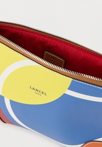 Πολύχρωμο πορτοφόλι LANCEL με κίτρινα και μπλε γεωμετρικά μοτίβα, καφέ δερμάτινες λεπτομέρειες και κόκκινη εσωτερική επένδυση. Διαθέτει κλείσιμο με φερμουάρ.