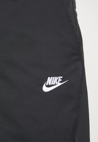 Svarta atletiska shorts med en slät textur som har en vit broderad Nike-logotyp på nedre vänstra sidan. Modern, strömlinjeformad design.