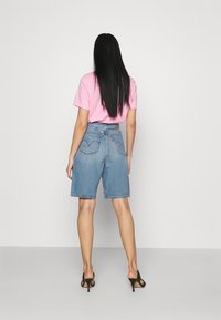 Pantalones cortos de denim azul claro con puños enrollados, bolsillos traseros y cintura alta. Combinados con una camiseta rosa ajustada y sandalias de tacón negro.